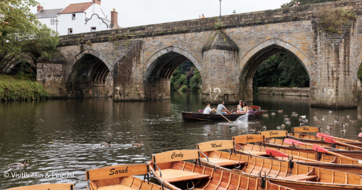 family in a rowing boat on the River Wear in Durham City with empty rowing boats in the foreground.